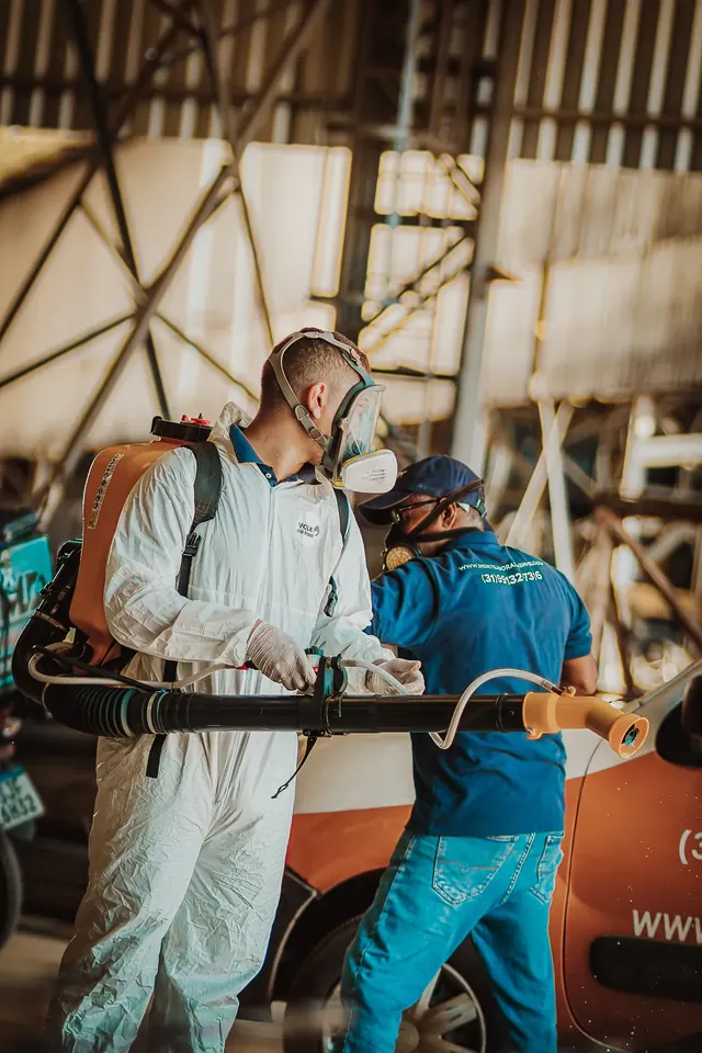 Dois profissionais preparando um equipamento costal ao lado do veículo da empresa.