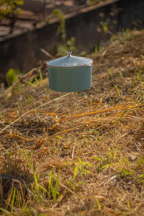 Recipiente azul com tampa instalado em uma haste sobre vegetação seca.