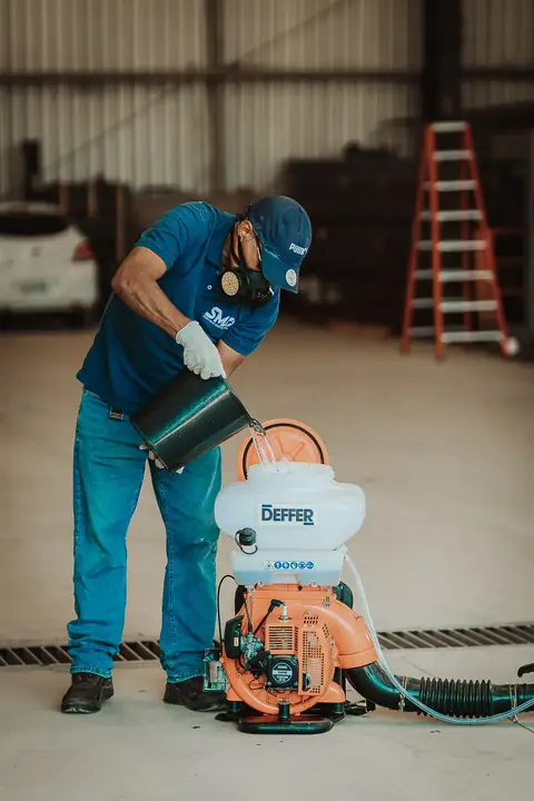 Profissional com uniforme azul da Senen Melo abastecendo um equipamento motorizado dentro de um galpão.