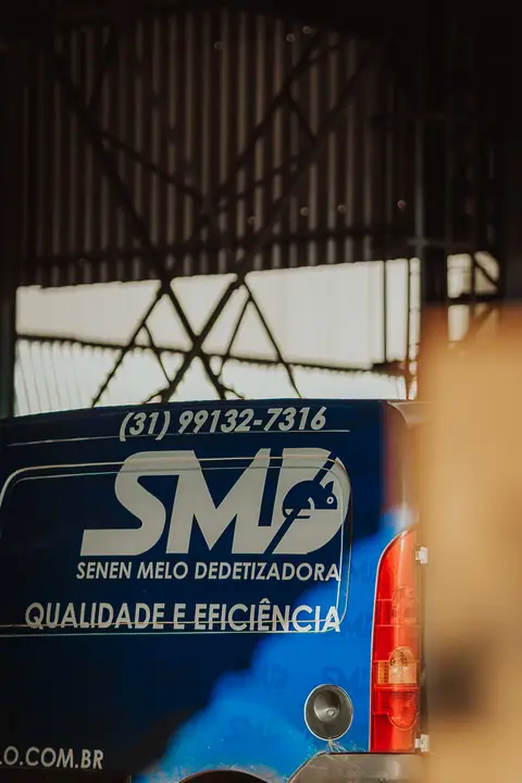 Traseira do veículo azul da Senen Melo, com logotipo, telefone e a frase “Qualidade e eficiência”, em área coberta.