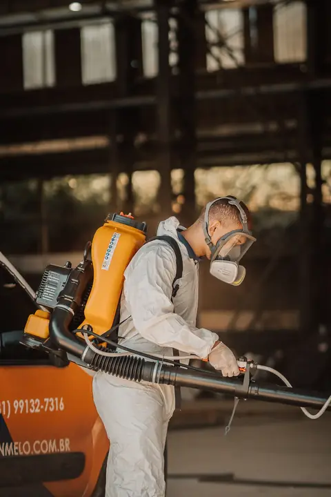Profissional de macacão e máscara facial com equipamento costal, ao lado do veículo da empresa.