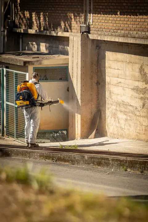 Profissional de macacão operando um equipamento costal junto à parede de um edifício.