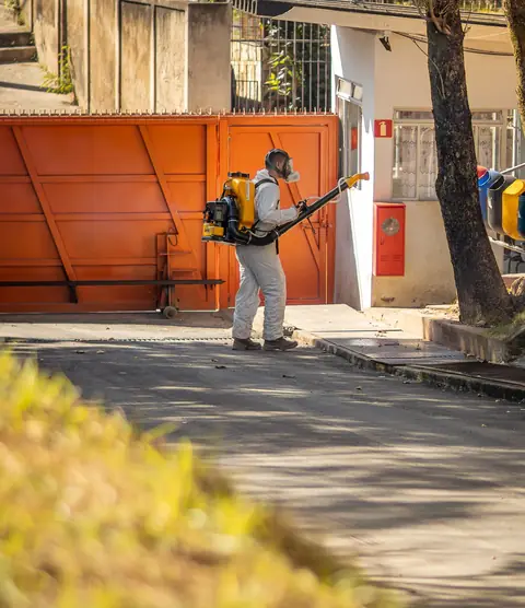 Profissional de macacão com equipamento costal em frente a um portão laranja.