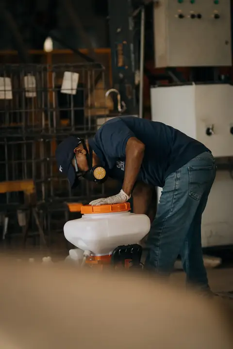 Profissional com uniforme azul-marinho, luvas e máscara manuseando o reservatório de um equipamento.