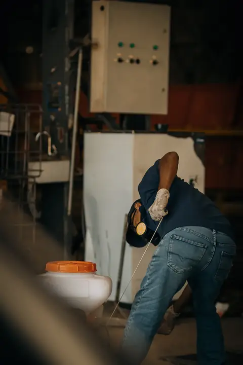 Profissional com uniforme azul-marinho ajustando um equipamento dentro de um galpão.