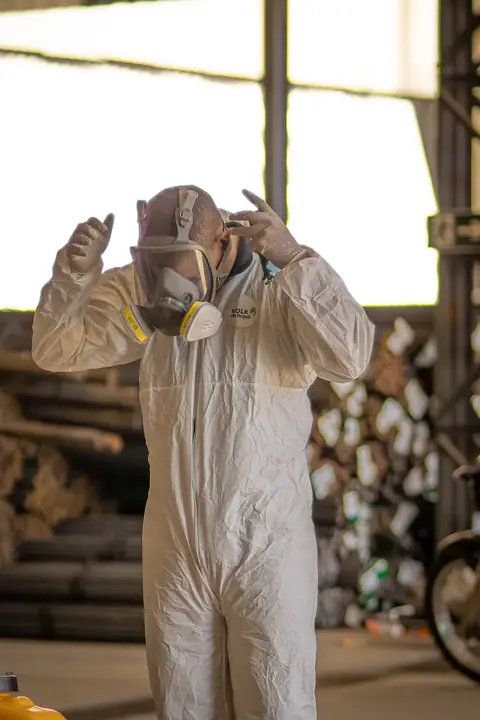 Profissional de macacão ajustando a máscara facial dentro de um galpão.
