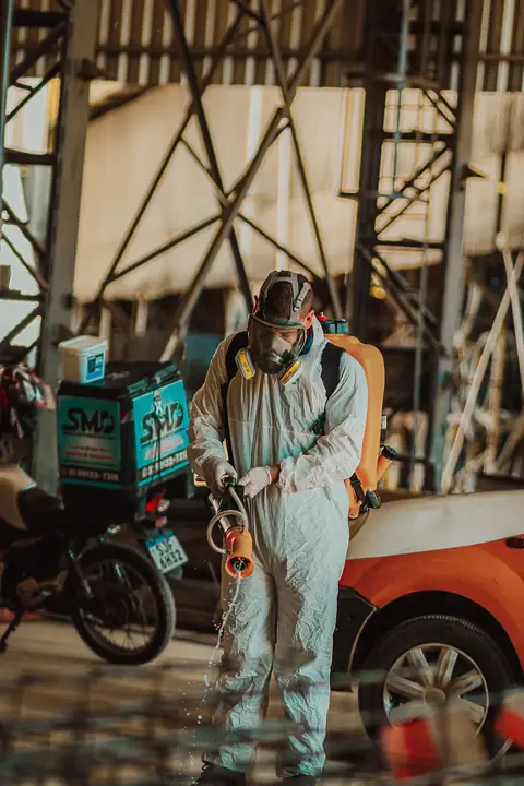 Profissional de macacão e máscara facial com equipamento costal, ao lado de uma motocicleta com baú SMD.