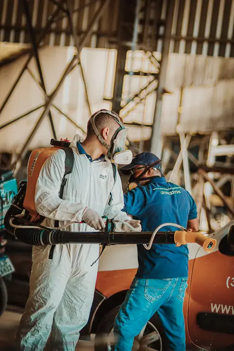 Dois profissionais preparando um equipamento costal ao lado do veículo da empresa.