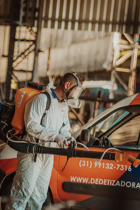 Profissional de macacão e máscara facial ajustando um equipamento costal ao lado do veículo da empresa.