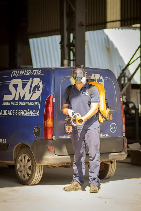 Profissional com uniforme da Senen Melo, máscara facial e equipamento costal em frente ao veículo da empresa.