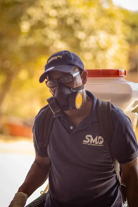 Profissional com uniforme da Senen Melo, boné, óculos e máscara respiratória.