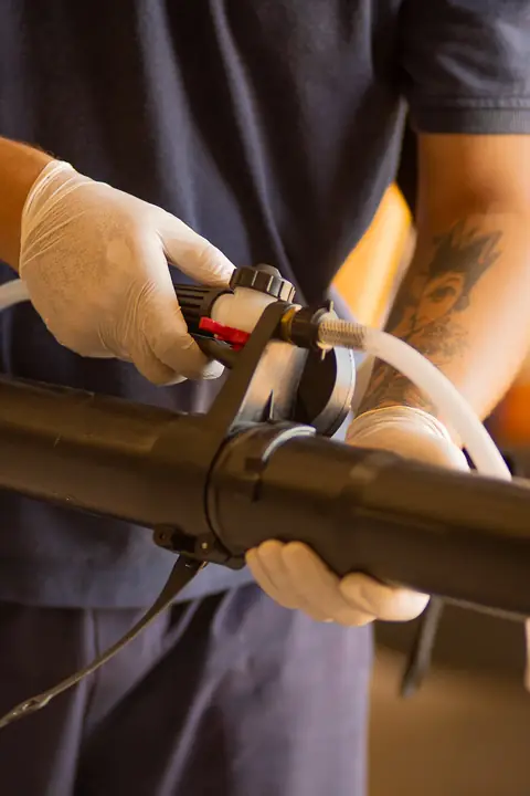 Profissional de uniforme e luvas segurando o tubo e o controle de um equipamento de aplicação.